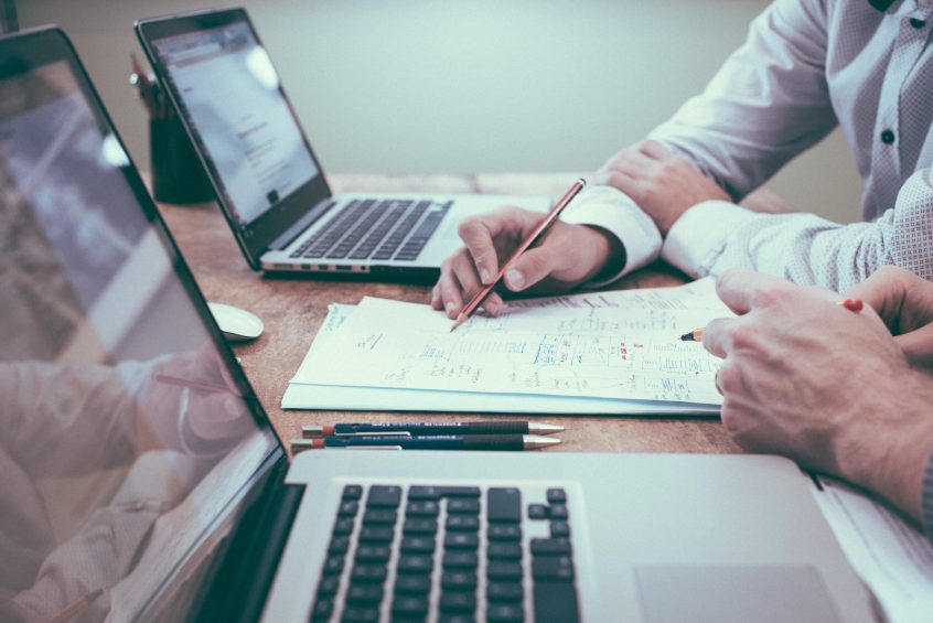 two people at a desk looking at paperwork with laptops open for car reimbursement program blog post
